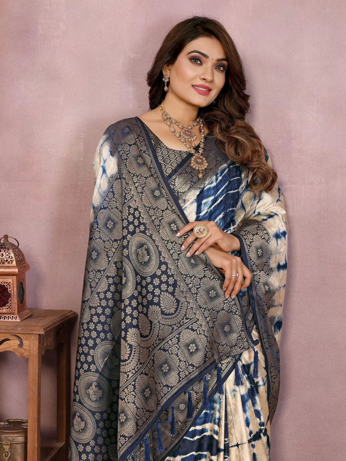 Woman wearing a traditional saree with intricate patterns against a pink background
